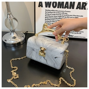 Detail of marble pattern acrylic clutch bag with golden horse handle and chain strap