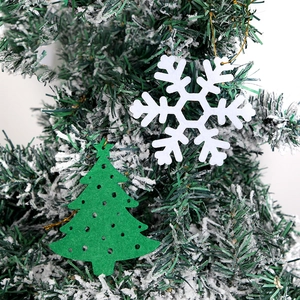 Detailed felt Christmas snowflake and tree ornaments with gold cords on snowy branch