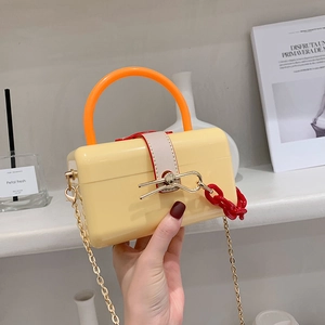 Yellow acrylic mini handbag with orange round handle and red chain strap held by hand