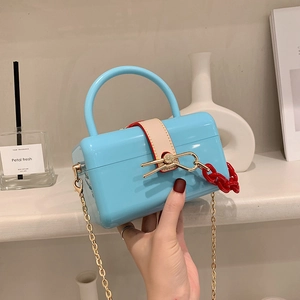 Bright blue acrylic box bag with gold accents and red chain on a minimalist shelf