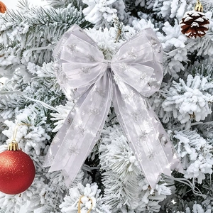Silver mesh Christmas bow with glitter snowflakes on a snow-covered pine tree