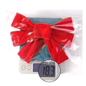 Detail of red velvet Christmas bow with gold trim in transparent packaging on scale