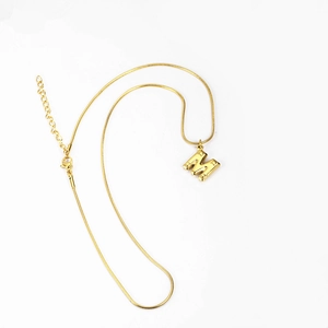 Macro detail of golden letter M pendant with textured dots and sleek snake chain