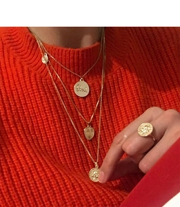 Détail de colliers superposés en pièces d'or avec visage abstrait sur pull orange