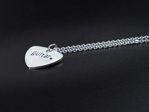 Macro shot of silver guitar pick pendant with brushed metal texture and guitar engraving
