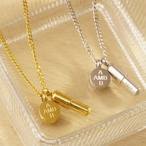 Detalle de colgantes de cápsula en oro y plata con disco grabado en cadenas de acero