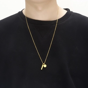 Collar con colgante de cápsula dorada y disco sobre modelo con suéter negro
