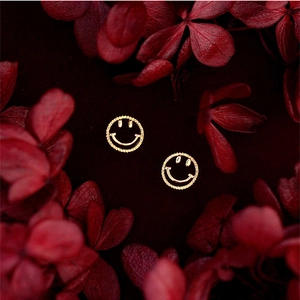 Gros plan de boucles d'oreilles smiley dorées avec bord perlé sur pétales rouges