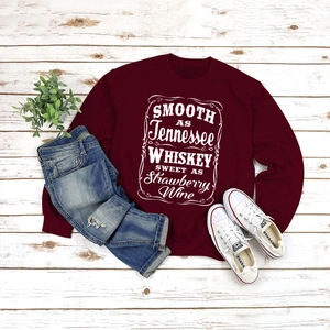 Detailed flat lay of burgundy sweatshirt with white lettering on white wood texture