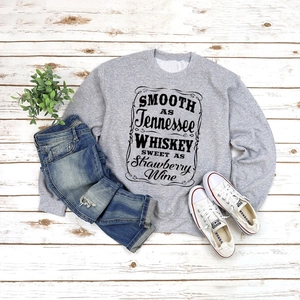 Flat lay of gray crewneck sweatshirt with Tennessee Whiskey print on wood floor