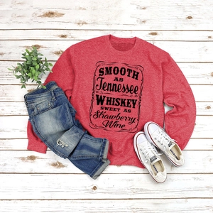 Flat lay of red crewneck sweatshirt with Tennessee Whiskey text print and jeans
