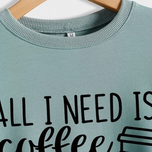 Mint green crewneck sweatshirt with 'ALL I NEED IS coffee' print on a wooden hanger