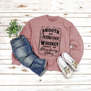 Flat lay of pink retro sweatshirt with Tennessee whiskey text on rustic wood background
