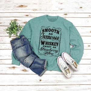 Flat lay of a teal crewneck sweatshirt with text paired with distressed blue jeans