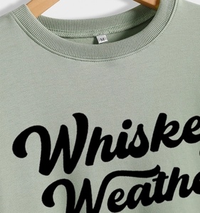 Detail of Whiskey Weather slogan print and M size label on sage green sweatshirt