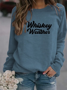 Close-up of Whiskey Weather script lettering on a casual blue-grey crewneck sweatshirt