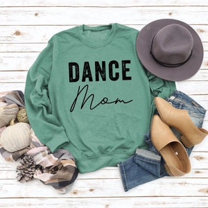 Flat lay of green DANCE MOM sweatshirt with autumn props and denim on white wood