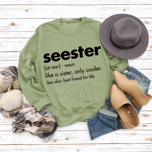 Flat lay of a sage green sweatshirt with seester print on white wooden floor