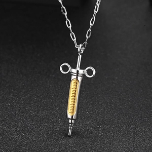 Macro detail of silver syringe pendant with gold engraved scales on a flat chain