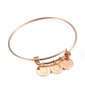 Close-up of rose gold adjustable wire bracelet with three engraved round letter charms