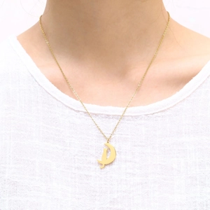 Detailansicht einer goldenen Halskette mit Halbmond und Katze auf einem Leinenhemd