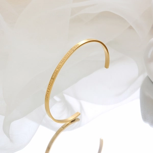 Minimalist gold C-shaped cuff bracelet with motivational engraving on reflective background