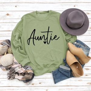 Flat lay of a green crewneck Auntie sweatshirt with casual accessories on a wooden floor