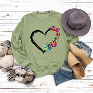 Light green crewneck sweatshirt featuring colorful paw print heart on white wood background