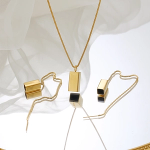 Close-up of geometric hollow cube pendant necklace and earrings set on reflective mirror