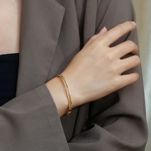 Macro detail of golden hollow-out cuff bracelet featuring TRAVEL AROUND THE engraved text