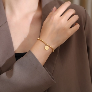 Dettaglio di un bracciale a sfere dorate con pendente Fu rotondo sul polso di una donna