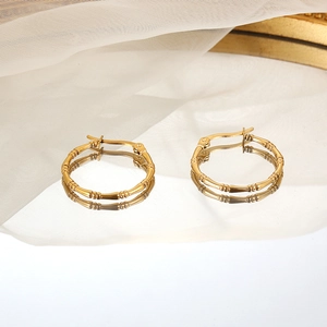 Minimalist gold-plated bamboo-style hoop earrings on a reflective mirror surface