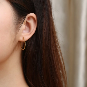 Close-up of golden bamboo hoop earrings worn by a model with a minimalist retro style