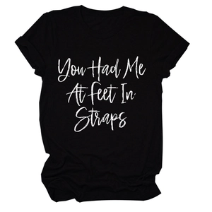 Dettaglio della stampa You Had Me At Feet In Straps su maglietta nera in cotone
