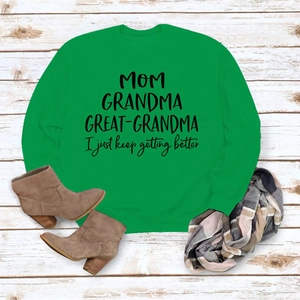 Détail du sweat-shirt vert vif avec slogan MOM GRANDMA sur fond de bois blanc