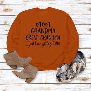 Détail de l'imprimé slogan MOM GRANDMA sur sweat-shirt orange sur fond en bois