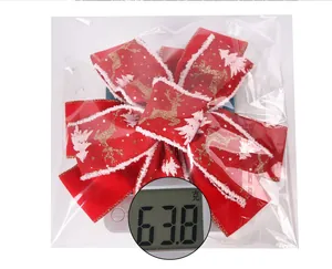 Detail of red Christmas bow with golden reindeer pattern being weighed on a scale