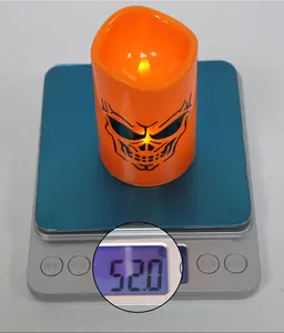 Detail shot showing an orange Halloween LED candle with skull print weighing 52g on scale