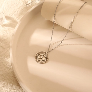 Détail du pendentif Om argenté avec texture soleil évidée sur une chaîne minimaliste