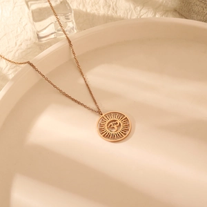 Gros plan du pendentif soleil symbole Om en or rose sur une assiette blanche