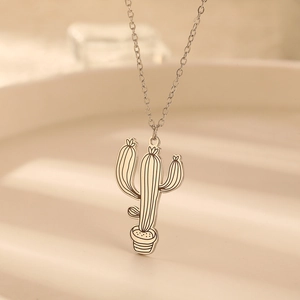 Macro d'un collier pendentif cactus argenté sur un support texturé blanc chaud