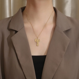 Détail d'un pendentif cactus doré sur une fine chaîne en acier titane portée par un modèle
