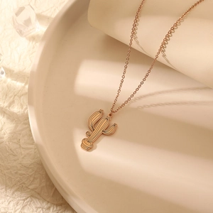 Gros plan d'un pendentif cactus en or rose avec une texture de ligne noire sur chaîne