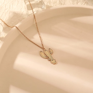 Collier avec pendentif cactus or rose minimaliste sur plateau crème avec lumière douce