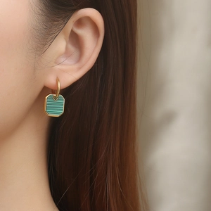 Close-up of gold octagon earrings featuring green malachite stone inlays on a model