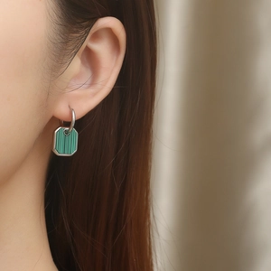 Close-up of a silver hoop earring with a green octagonal striped pendant on a model