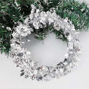 Close-up of silver Christmas tinsel garland with holly leaf cutouts for party decor