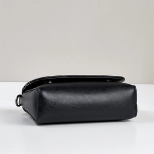 Detail view of black pebbled leather texture, metal D-ring and magnetic closure on handbag