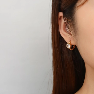 Dettaglio di un orecchino a cerchio dorato con zircone rotondo indossato da una donna