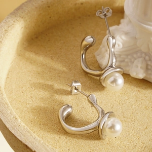 Detailed close-up of liquid metal silver earrings with white pearls on stone tray